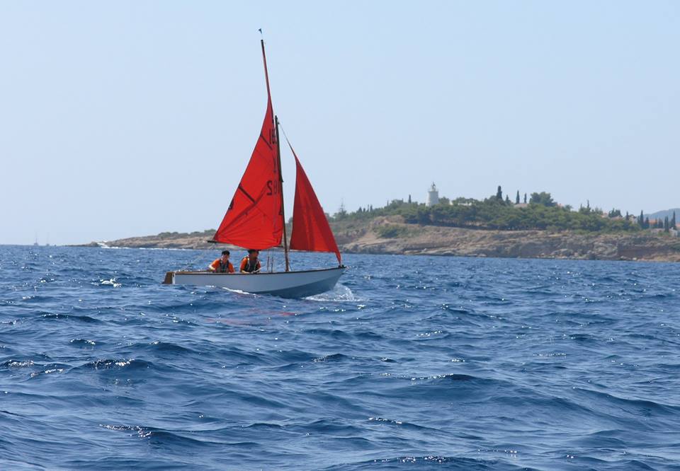 A white wooden Mirror dinghy sailing on a blue sea on a sunny day