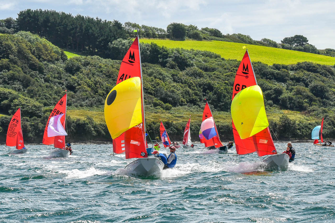 A white Mirror dinghy leading the fleet under spinnakers